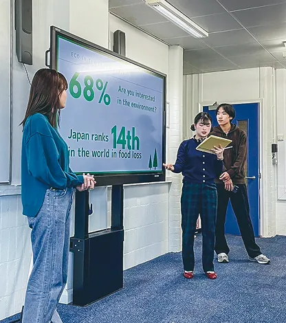 ディスプレイの前で環境問題について発表する学生たち