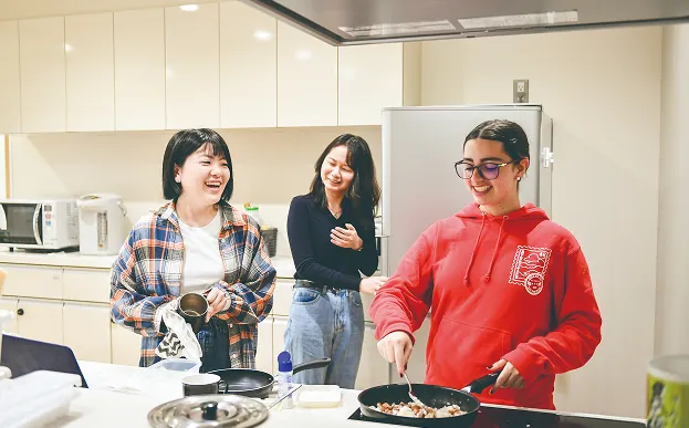 キッチンスペースで楽しそうに料理をする3人の女子学生たち