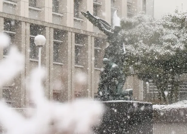雪が激しく降る冬の大学キャンパスと白く雪が積もった人物の彫刻像