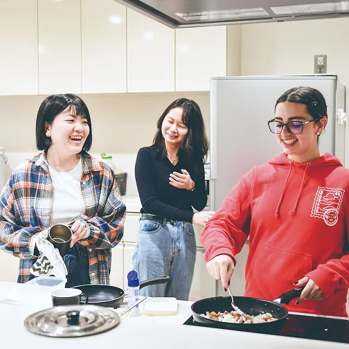キッチンで料理をしながら笑顔で会話する3人の女子学生