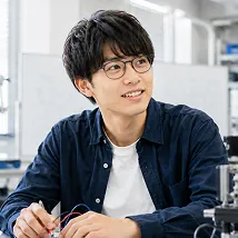 実験器具の近くで笑顔を見せるメガネの男子学生