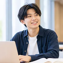 パソコンに向かって笑顔を見せる男子学生