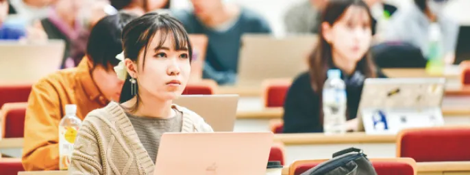 講義室でノートパソコンを使って真剣に学ぶ学生たち