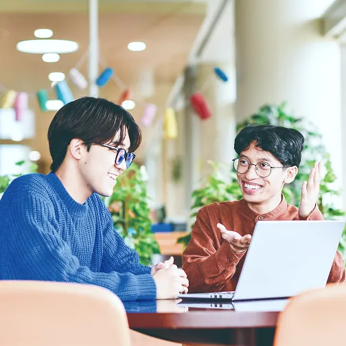 ノートPCを見ながら笑顔で会話する2人の男子学生