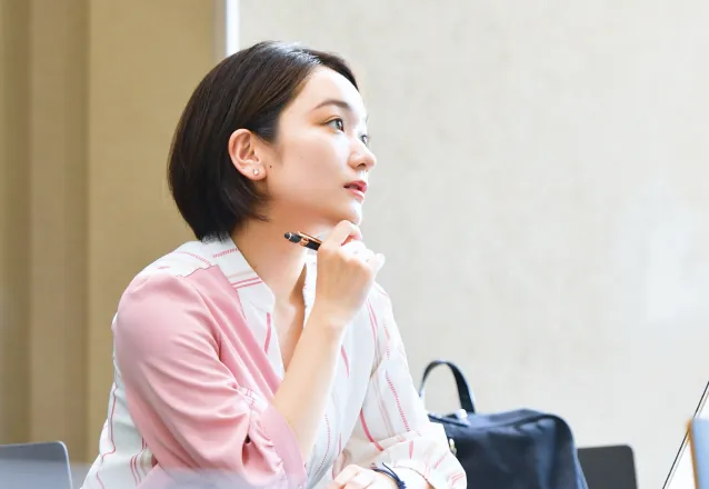 ペンを顎に当てて真剣に斜め上を見つめながら思考する女性の横顔