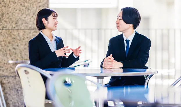 スーツ姿で向かい合い、笑顔で会話をする若い男女
