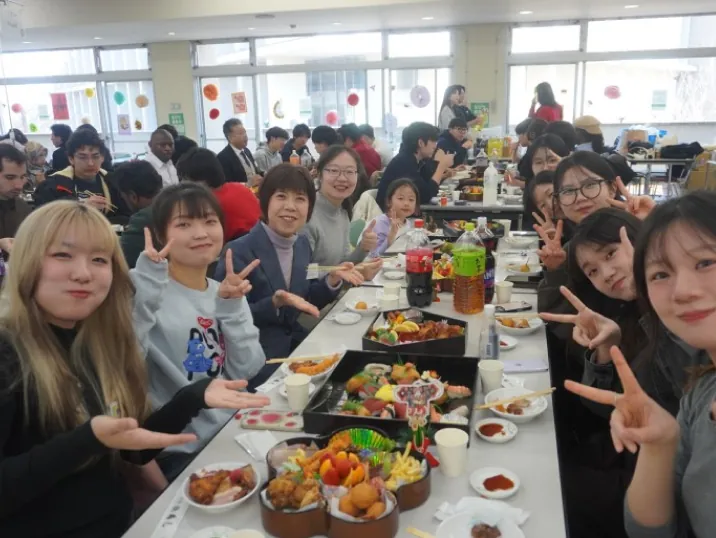沢山の料理が並ぶ食堂のテーブルを囲み、笑顔でポーズをとる学生たち